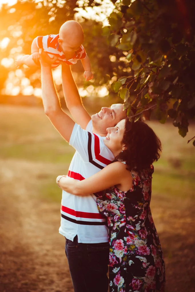 cheerful-parents-hold-their-little-son-up-standing-outside-th